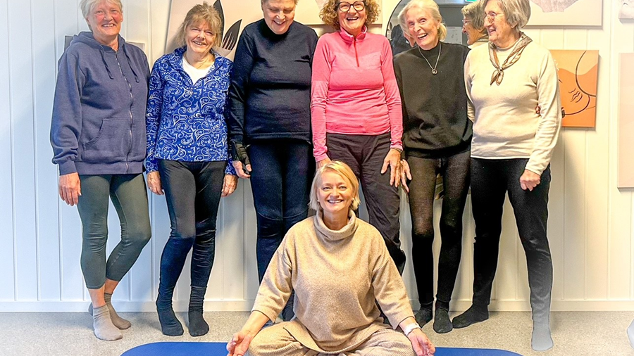 Bilde av 7 smilende mennesker som står rundt en yogamatte