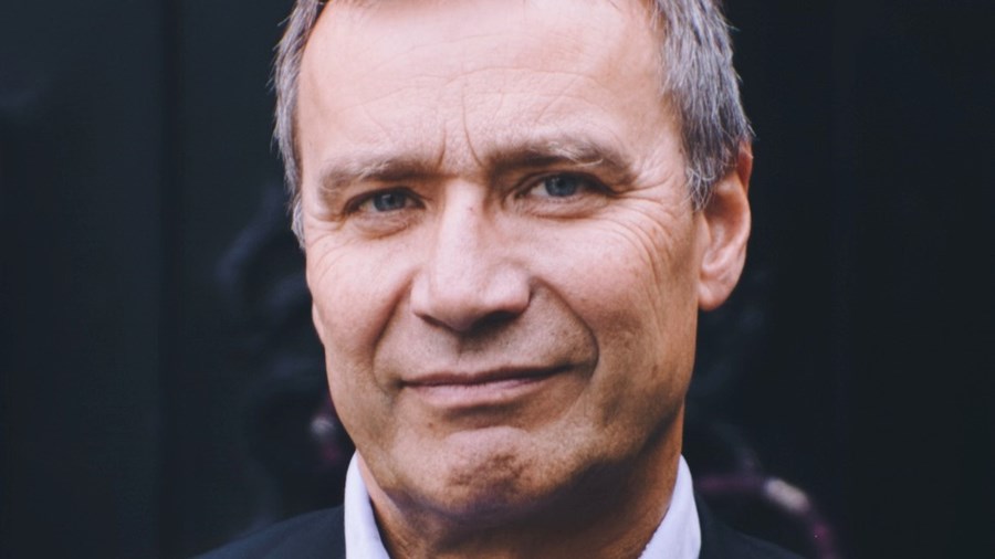 Mann med mørk jakke og lys skjorte smiler inn i kamera.